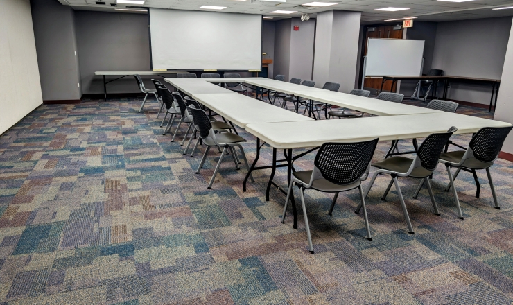 Meeting Room 3 - Open table square surrounded by chairs, large screen lowered and white board